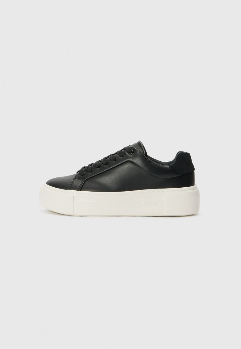 Sneaker en cuir noir avec un bout arrondi, semelle plateform blanche et lacets noirs. Présente un logo discret au niveau du talon et une texture lisse.