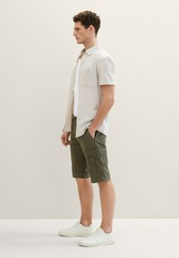 Camisa de botones de manga corta en gris claro, pantalones cortos cargo verde oliva con bolsillos y zapatillas blancas. Diseño simple y funcional en colores suaves.
