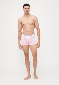 Roza bombažne boksarice z belim pasom, na katerem je črno besedilo. Boksarice imajo oprijet dizajn in gladko teksturo.