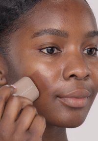 Beige Cremestift, der auf die Wange aufgetragen wird, zeigt eine glatte Textur und leichten Glanz, vor einem Hintergrund mit natürlichem Hautton.