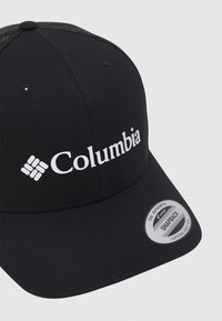Fekete snapback sapka hálós háttal, elöl fehér "Columbia" logóval, az oldalon pedig egy kör alakú márkajellel.