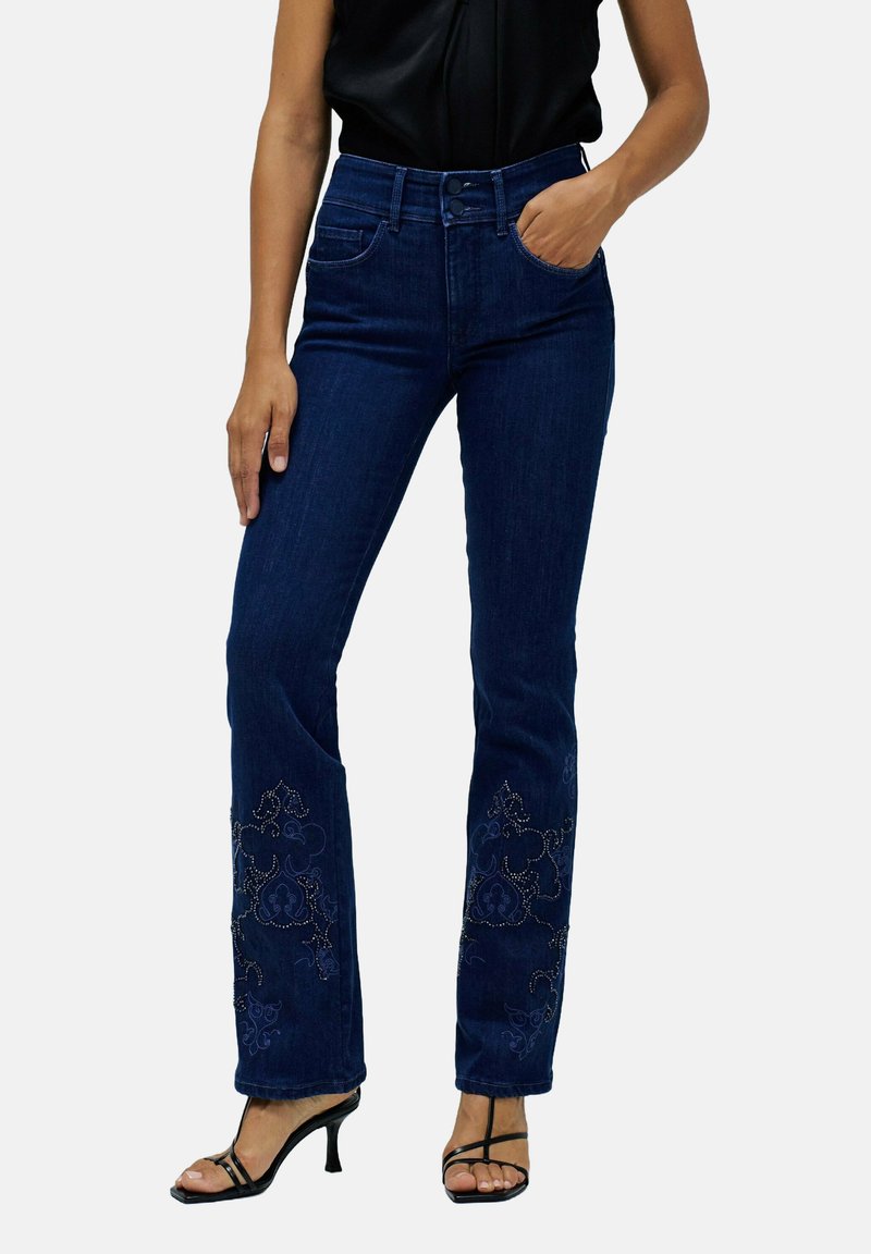Jean bleu foncé au design ajusté, avec des broderies florales et des accents de perles à l'ourlet, complétés par des talons noirs à lanières.