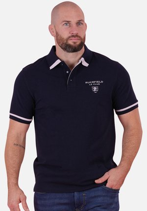 Polo marine avec des accents blancs, doté d'un col et de manches courtes. Comprend un logo brodé sur la poitrine. Texture de tissu lisse.