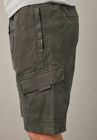 Sötétzöld cargo short, textúrált anyagból, több zsebbel, cipzáras részletekkel és laza, kényelmes fazonban.