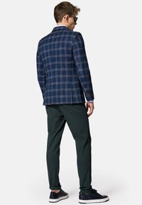 Niebiesko-granatowy marynarka w kratę z jasnoniebieskimi akcentami, zestawiona z ciemnozielonymi spodniami. Model w ciemnych butach, widziany z tyłu.