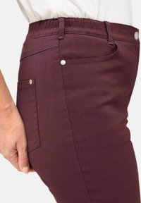 Bordeaux rekpantalon met een tailleband, zijzakken en drukknoopaccenten. Glad textuur met een getailleerde pasvorm.