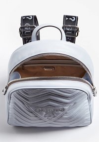 Světle modrý batoh vyrobený z texturované umělé kůže, se štepovaným vzorem, stříbrnými detaily a logem. Vnitřek má béžovou podšívku.