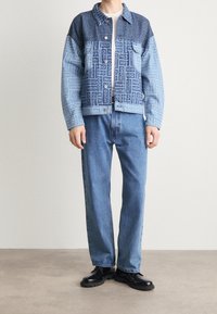 Kurtka dżinsowa w niebieskich odcieniach z wzorzystą górną częścią, zapięciami na guziki i luźnym krojem. Połączona z jasnoniebieskimi jeansami i czarnymi butami.