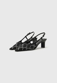 Black slingback heels made of smooth material, featuring a pointed toe and embellished with silver rhinestone patterns. Mid-block heel.
