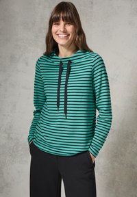 Sweatshirt à capuche rayé vert et noir avec une coupe décontractée, doté d'un cordon de serrage et de manches longues. Porté avec un pantalon noir.