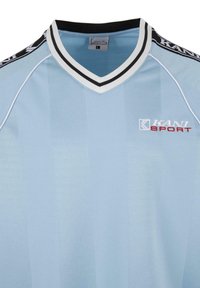 Šviesiai mėlynos spalvos sportinis marškinėlis su V formos iškirpte, balta ir juoda juostelė aplink apykaklę, raudonas KANI SPORT logotipas. Audinyje yra vertikalios juostos.