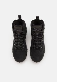 Des bottes de randonnée noires avec une tige en suède texturé et en tissu, des lacets ronds, une coupe haute et une semelle en caoutchouc robuste avec des crampons profonds.