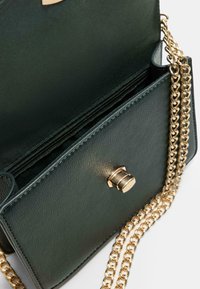 Grüne Leder-Umhängetasche mit goldener Kettenriemen, ausgestattet mit einem oberen Verschluss und einem Reißverschlussfach. Glatte Textur mit minimalen Nahtdetails.