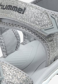 Silverglittrande sandaler med mjukt tygfoder, justerbara remmar och en strukturerad sula. Varumärket "hummel" är synligt på remmen.