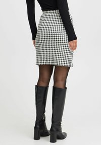 Sort og hvid houndstooth mini nederdel med en tætsiddende form, høj talje, og struktureret vævning, parret med lange sorte læder støvler med hæl.