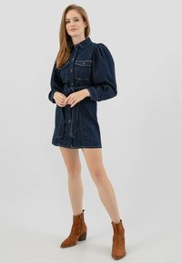 Sukienka dżinsowa z kołnierzykiem, bufiastymi rękawami i paskiem w talii. Głęboki niebieski kolor, z kieszeniami z przodu i kontrastowymi przeszyciami.