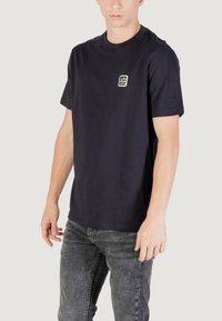 T-shirt in cotone blu navy con scollo rotondo, maniche corte e un piccolo logo grafico nella zona del petto. Morbido al tatto, vestibilità rilassata.