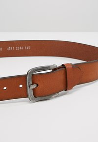 Bruine leren riem met een gestructureerde afwerking, voorzien van een zilverkleurige metalen gesp en meerdere verstelgaten langs de lengte.