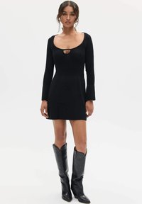 Czarna, prążkowana mini sukienka z okrągłym dekoltem i detalem w formie dziurki. Długie rękawy z rozkloszowanymi mankietami, zestawione z wysokimi czarnymi botkami.