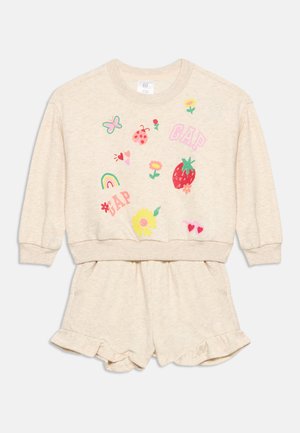 Σετ παιδική φόρμας σε μπεζ χρώμα με πολύχρωμα σχέδια που περιλαμβάνουν φράουλα, πασχαλίτσα, πεταλούδα, λουλούδια, ουράνιο τόξο, καρδιές και το κείμενο "GAP".