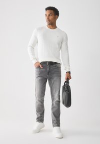Pull blanc à côtes, jean gris et baskets blanches. Tenant un sac à main noir texturé. Tenue décontractée avec une silhouette ajustée.