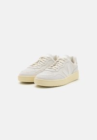 Beige mockaskor med en strukturerad design, rund tå och krämfärgad gummisula. Har snörning och logodetalj på sidan.