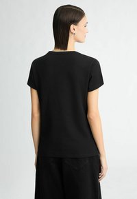 Zwarte katoenen t-shirt met korte mouwen, een ronde halslijn en een relaxte pasvorm, gedragen met donkere spijkerbroek, gezien vanuit de achterkant.