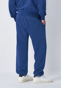 Blauwe joggingsbroek van een zachte stof met een relaxte pasvorm, voorzien van zijzakken en elastische boorden, gecombineerd met witte sneakers.