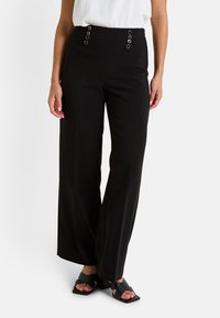 Pantalones de pierna ancha negros, hechos de una tela suave, con detalles de botones en el frente, bolsillos laterales y un corte entallado. Combinados con sandalias negras de tacón bloque.