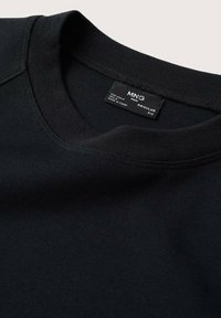 Sort crewneck sweatshirt med en glat tekstur og ribbet krave. Indeholder en synlig etiket, der angiver størrelse og plejeinformation.