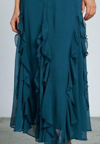 Abito maxi fluido di colore teal, realizzato in tessuto leggero, caratterizzato da strati arricciati lungo i lati e una texture liscia, vicino all'orlo.