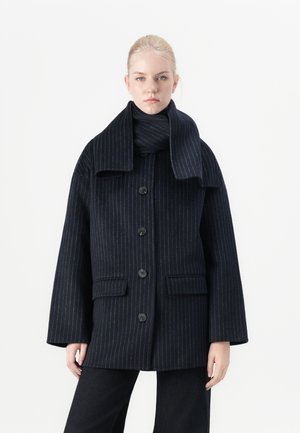 Veste en laine à rayures marines avec de grands boutons, deux poches avant et un large col, accompagnée d'une écharpe assortie.