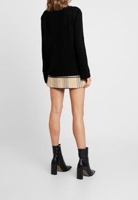 Maglione nero a coste con maniche lunghe, abbinato a una minigonna beige a quadri. Completano il look stivaletti neri con tacco.