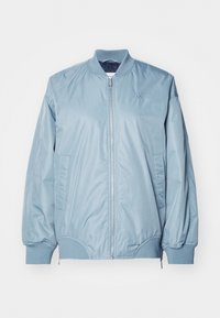 Svetlomodrá bomber bunda vyrobená z hladkej, lesklej tkaniny. Obsahuje zips vpredu, rebrovaný golier, elastické manžety a bočné vrecká. Malý detail loga.