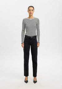 Stripet svart og hvit langermet topp, sammen med høyt liv svarte denim jeans, med et svart belte og spisse svarte hæler.