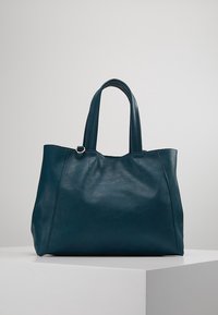 Tyrkysově modrá kožená taška přes rameno se dvěma uchy, texturovaným povrchem a minimalistickým designem. Má centrální šev a žádné další ozdoby.