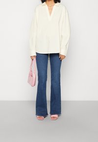 Chemise crème clair à manches longues avec un décolleté en V profond, associée à un jean flare bleu. Tenant un sac à main rose brillant et portant des sandales à talons roses.