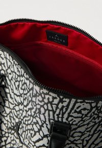 Mala com padrão a preto e branco, forro interior vermelho, fecho de correr suave e etiqueta da marca, concebida em forma retangular.