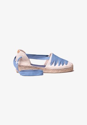 Chaussure espadrille beige avec semelle en jute tressée, lacets en tissu bleu enroulés autour de la cheville, et détails triangulaires en tissu bleu sur l’avant.