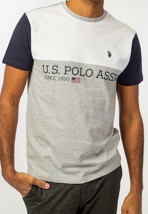 Mann trägt ein kurzärmeliges Farbblock-T-Shirt in Weiß, Marineblau und Grau mit der Aufschrift "U.S. POLO ASSN" auf der Brust.