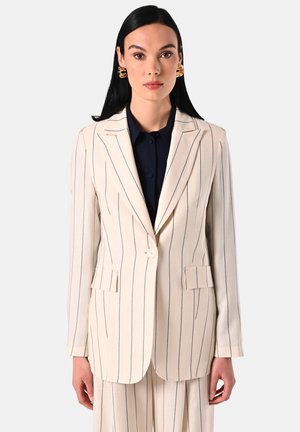 Beige pinstripe blazer met notch-lapels, enkele knoopsluiting, twee voorkruinen en een gladde textuur. Ggedragen over een donker shirt.