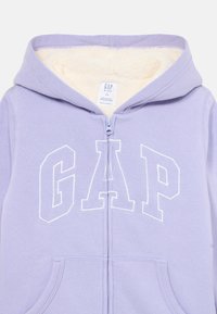 Felpa zip-up per bambini di colore lavanda con fodera in pile bianco, tasche frontali e logo GAP bianco ricamato sul petto.