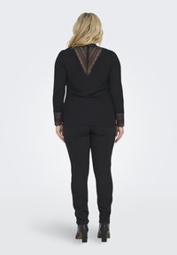 Black long-sleeve top with lace detailing at the back and cuffs paired with black fitted pants and heeled boots. Smooth texture throughout.