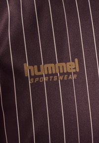Lilla sportststof med hvide lodrette striber; har logoet "hummel SPORTSWEAR" i guld. Glat tekstur, moderne design.