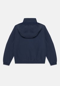 Veste coupe-vent bleu marine, matériau léger, poignets élastiques, capuche ajustable et coupe décontractée. Design simple, sans motifs ni accessoires visibles.