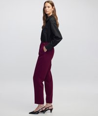 Camisa negra de botones con un bolsillo en el pecho, combinada con pantalones ajustados burdeos. Los zapatos son negros con una correa al talón y punta afilada.