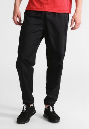 Schwarze Sporthose mit lockerer Passform, ausgestattet mit einer glatten Textur und einem elastischen Bund. Kombiniert mit schwarzen Mesh-Sneakern.