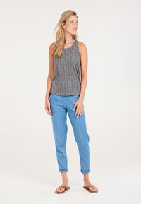 Canotta grigia a fantasia con vestibilità ampia, abbinata a pantaloni tapered azzurri chiari e infradito marroni. Outfit semplice e casual.