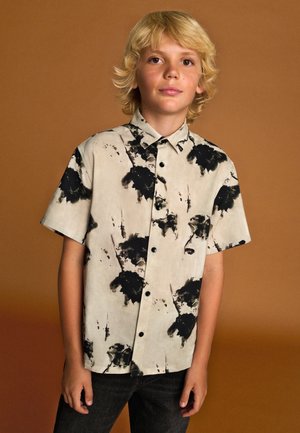 Kortærmet skjorte med knapper i lys beige med sort abstrakt sprøjtet mønster. Bomuldsstof, klassisk krave og sorte knapper.
