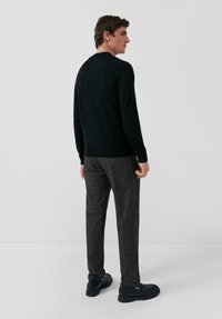 Czarny dzianinowy sweter z okrągłym dekoltem, zestawiony z szarymi spodniami w kratę i czarnymi mokasynami, tworzący swobodny, a jednocześnie uporządkowany wygląd.